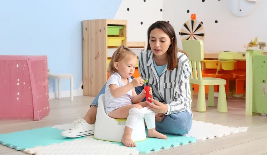 Anne, lazımlıkta oturan küçük çocuğuyla oyuncakla oynayarak tuvalet eğitimini destekliyor — çocuklarda tuvalet eğitimi nasıl verilir