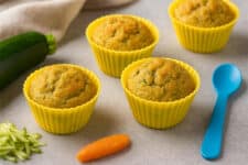 Kabaklı tam buğday unlu bebek muffin (9 Ay+), sarı silikon kalıplarda pişmiş mini muffinler, yanında kabak rendesi ve mavi bebek kaşığı