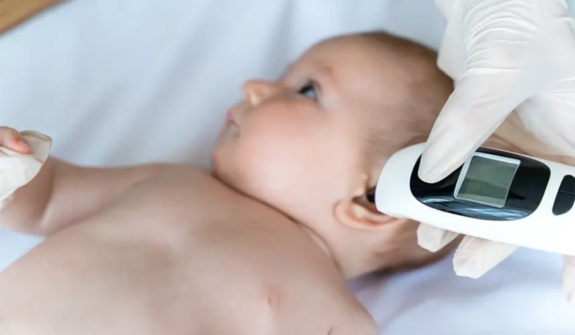 Sağlık çalışanı, aşı sonrası bebeğin ateşini dijital termometreyle ölçüyor.