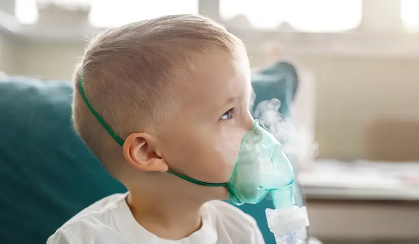 Nebulizatör cihazıyla tedavi gören çocuk — solunum güçlüğü yaşayan küçük bir çocuk ev ortamında buhar tedavisi alıyor.