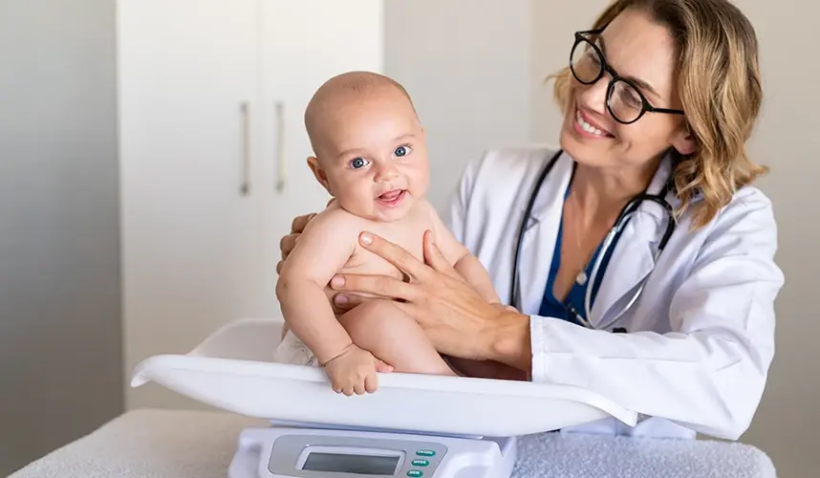 Bebek doktor kontrolünde tartılırken gülümserken, kilo ve boy ölçümü sırasında sağlık takibi yapılan bir bebek.